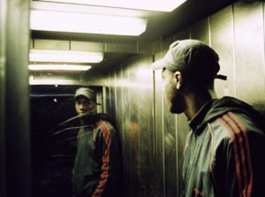A man in a hat and jacket standing next to a mirror.