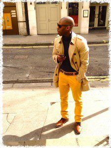 A man in yellow pants and sunglasses standing on the sidewalk.