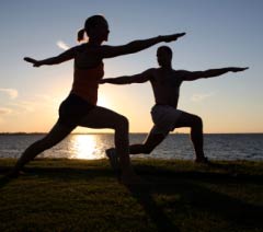 A man and woman doing yoga on the beach.